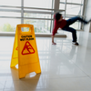 Person slipping on wet floor with a caution sign in the foreground