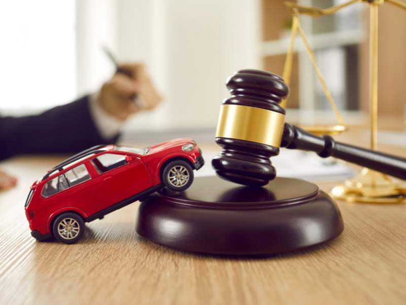 car accident lawyer talking in the background with a gavel with a red toy car on top in the foreground